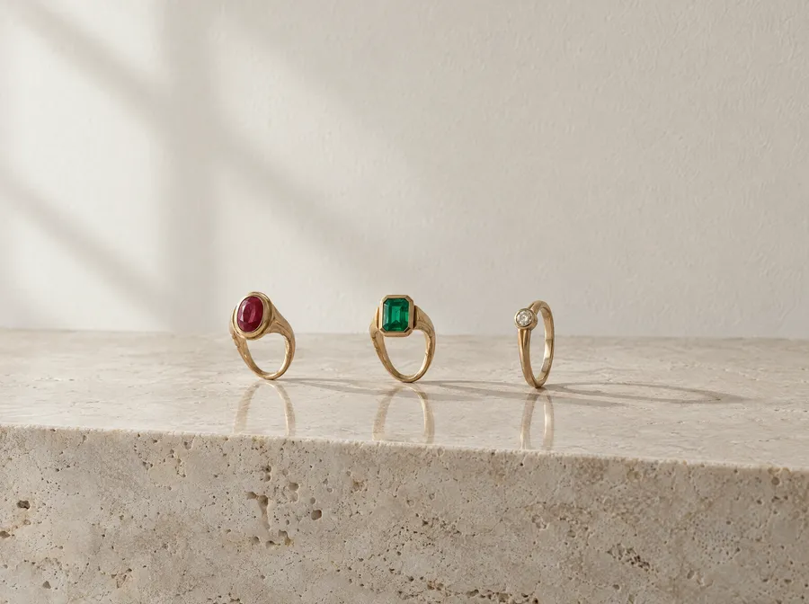Drei alte Goldringe mit Rubin, Smaragd und kleinem Diamant, aufrecht auf einer Kante aus hellem Travertin